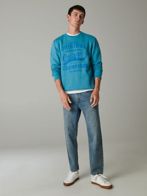 Man wearing a blue sweatshirt and jeans on a gray background