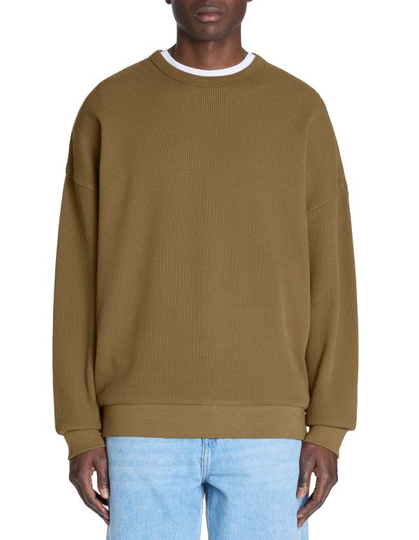 Person wearing a brown ribbed sweater and light blue jeans on a white background