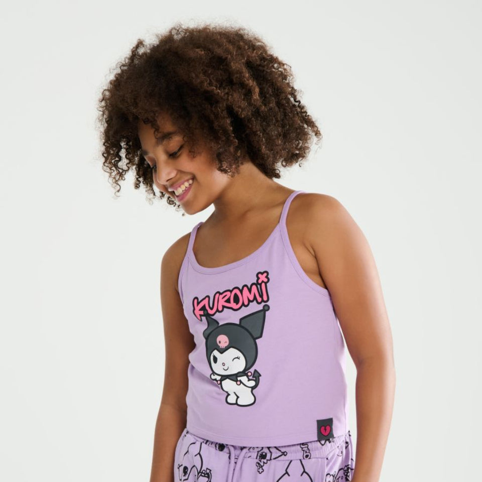 A young girl with curly brown hair wearing a light purple two-piece pajama set featuring a Kuromi cartoon graphic on the tank top and an all-over Kuromi print on the shorts, set against a plain light gray background.