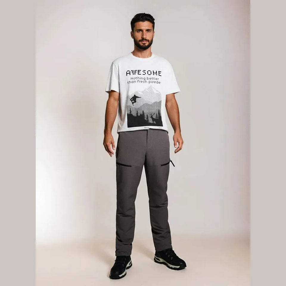 A man modeling a white graphic t-shirt and dark gray outdoor pants against a plain beige studio background.