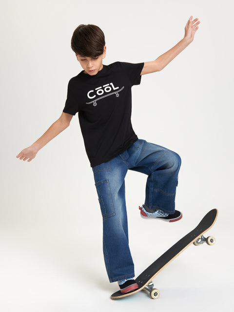 Child wearing a black t-shirt with 'Cool' printed on it, standing on a skateboard.
