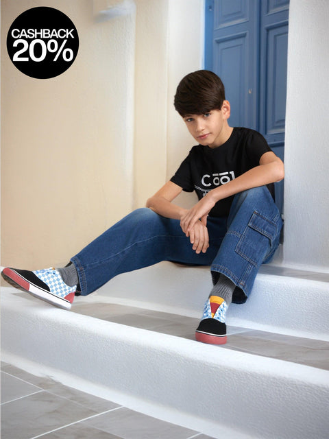 Young boy sitting on steps wearing a black t-shirt, blue jeans, and colorful socks.