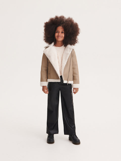 Child wearing a beige and white jacket with black pants on a white background