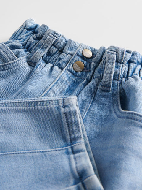 Close-up of blue denim jeans with buttons and stitching details on a light gray background
