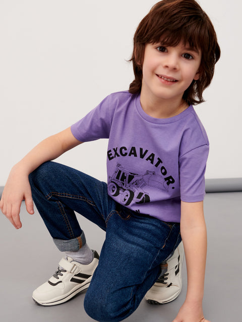 Child wearing a purple t-shirt with 'Excavator' print, sitting on a gray surface.