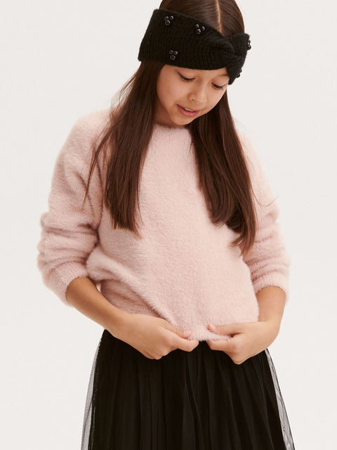 Person wearing a pink sweater and black headband with decorative buttons on a white background