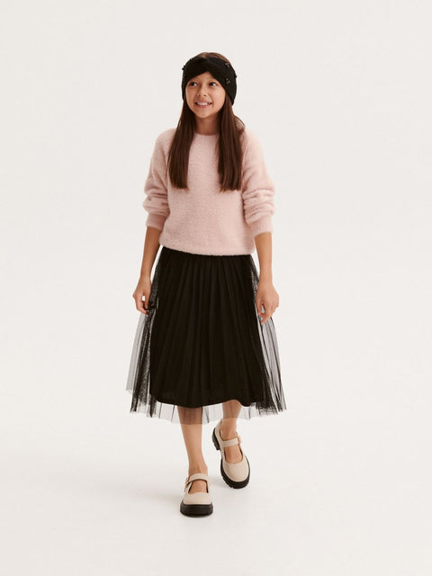 Young girl wearing a pink sweater and black tulle skirt on a white background
