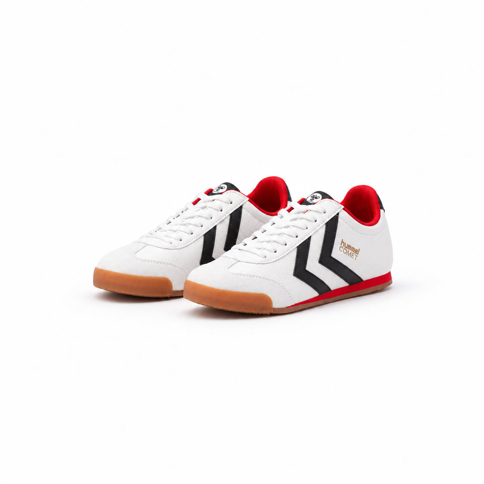 A pair of Hummel Corret low-top sneakers in white leather with black chevron stripes, red accents on the collar and midsole, and gum soles, shown on a white background.
