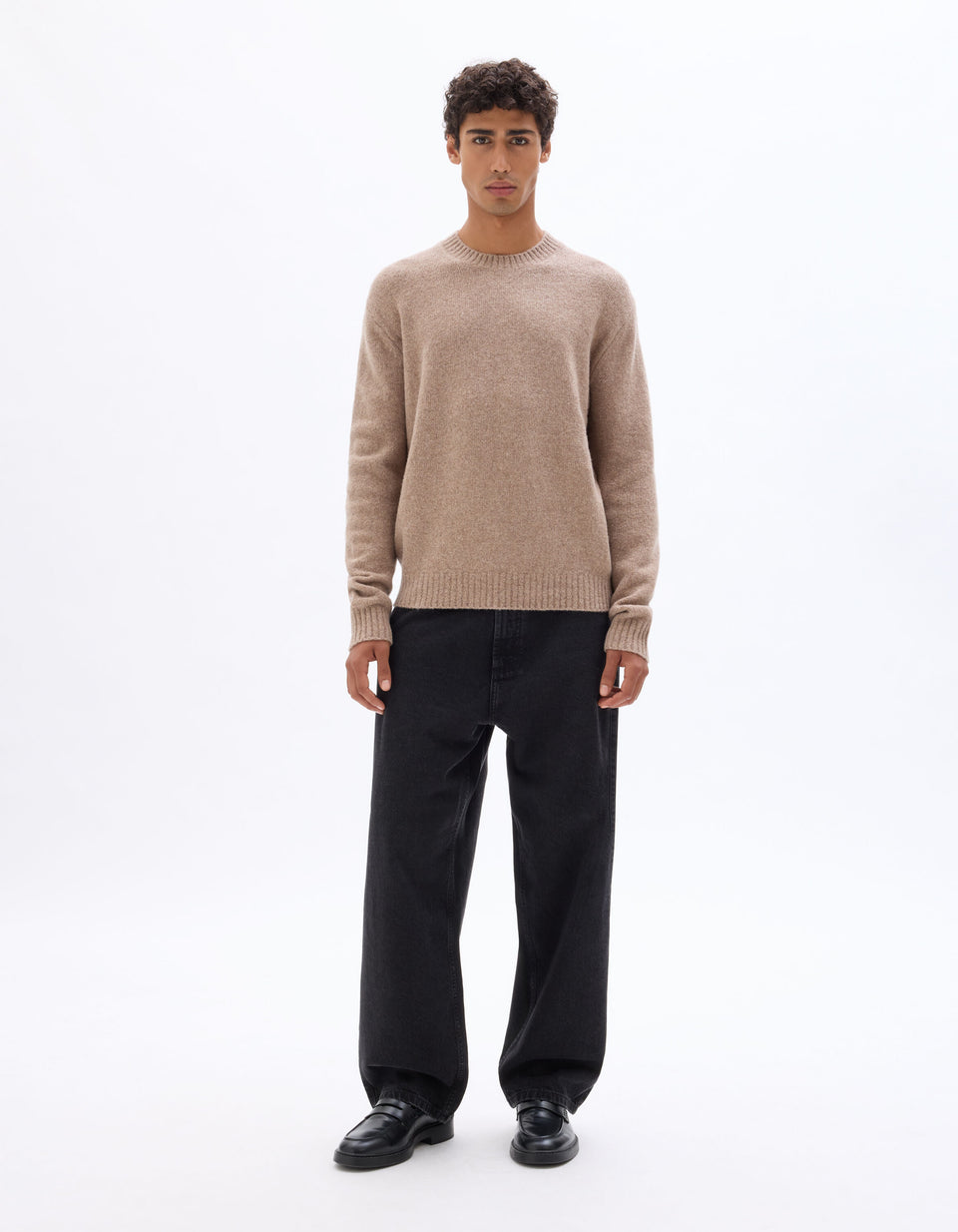 Man wearing a beige sweater and black pants on a white background