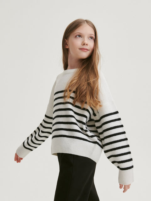 Young girl wearing a black and white striped sweater on a plain background