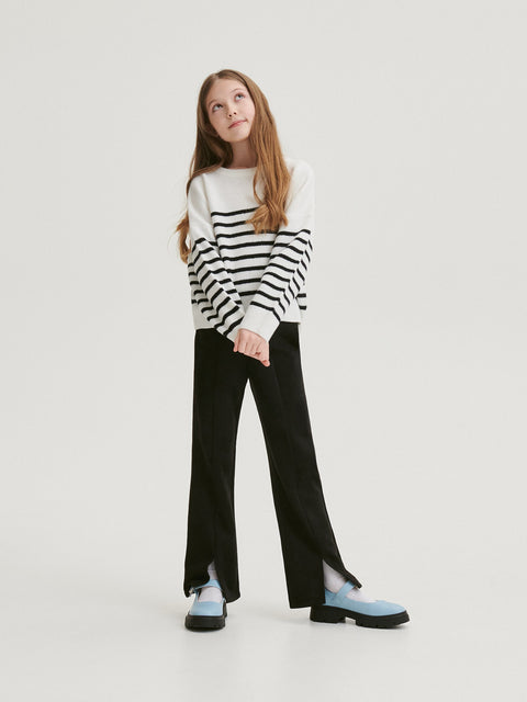 Person wearing a black and white striped sweater with black pants on a white background
