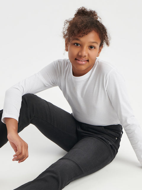 Person wearing a white long-sleeve top and black pants sitting on a white surface.