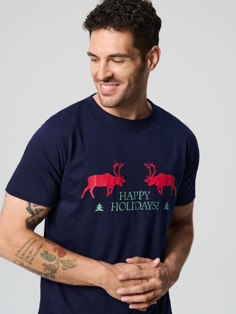 Man wearing a navy blue t-shirt with red reindeer and 'Happy Holidays!' text on a light gray background