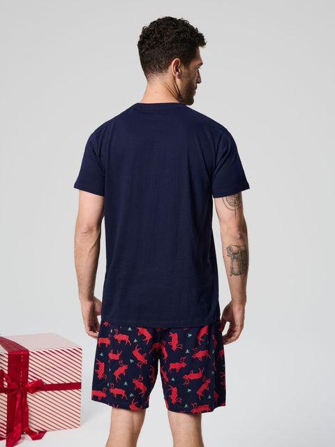 Man wearing navy t-shirt and red and blue patterned shorts with a gift box on a light gray background