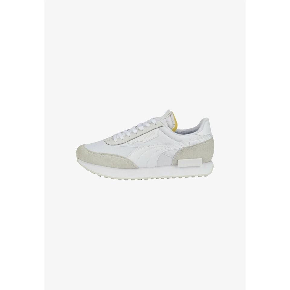 A white low-top sneaker with light beige suede overlays on the toe and heel, white laces, and a small yellow accent on the tongue, shown against a plain white background.