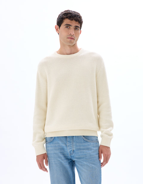 Man wearing a cream sweater and blue jeans on a white background