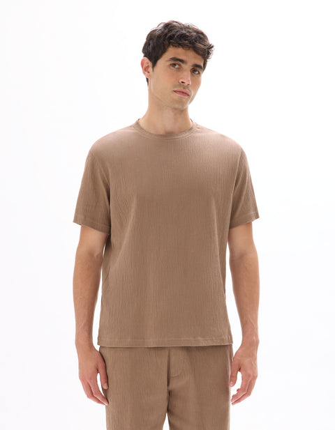 Man wearing a brown ribbed t-shirt and pants on a white background