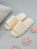 Pair of beige slippers on a gray surface with decorative pink flowers and pearls.