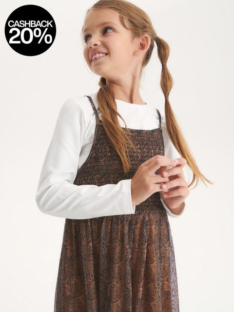 Young girl wearing a brown checkered pinafore dress over a white shirt on a white background