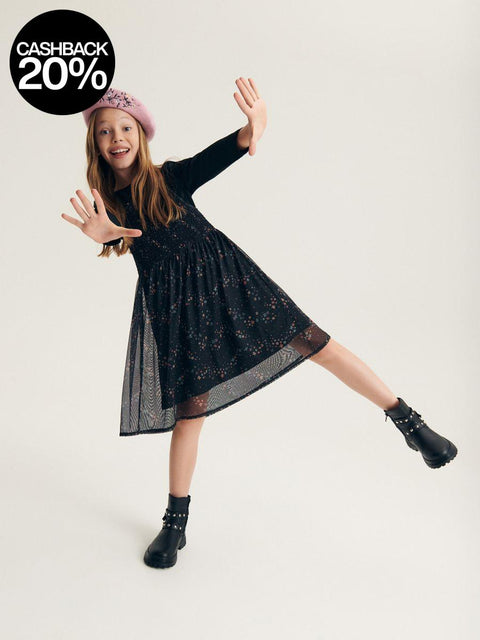 Young girl in a black dress and boots posing against a white background