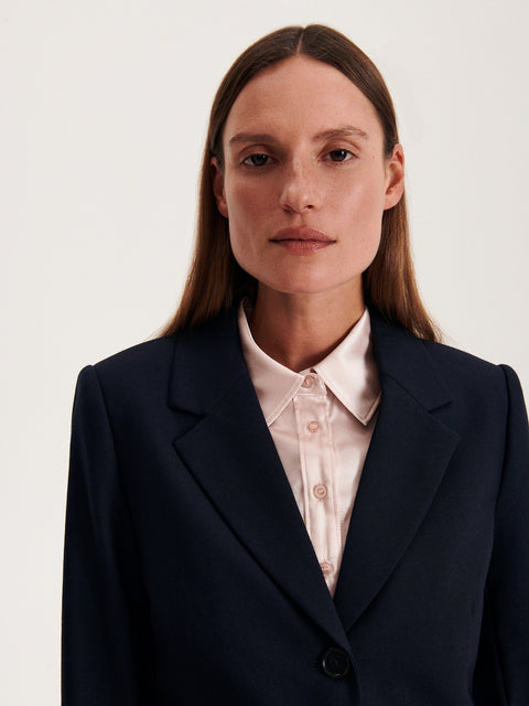 Woman wearing a navy blazer over a light-colored shirt on a plain background