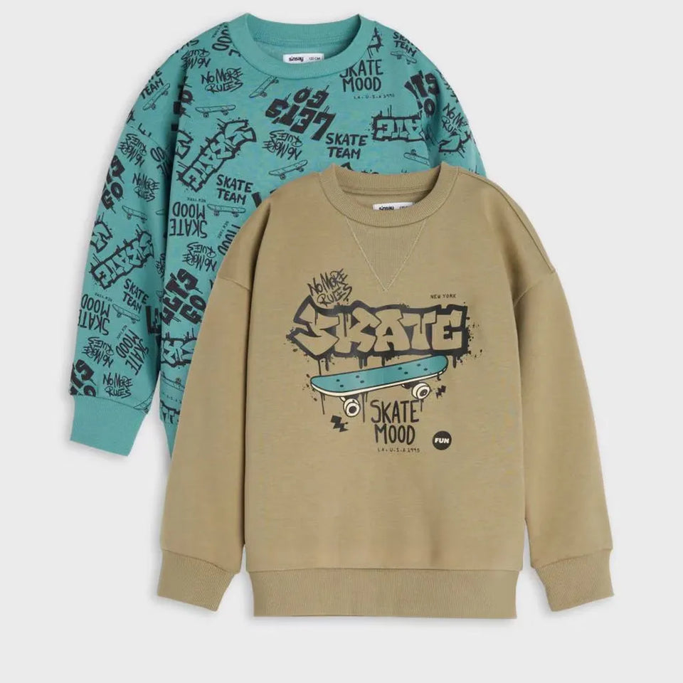 Two kids' crewneck sweatshirts from Skate Club, one in teal with black graffiti-style text and the other in tan with a large central skateboard graphic, displayed against a light gray background.