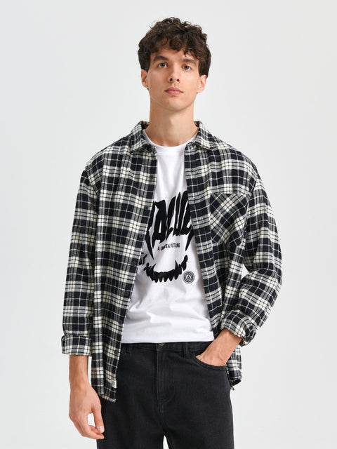 Man wearing a black and white plaid shirt over a white graphic t-shirt on a light gray background