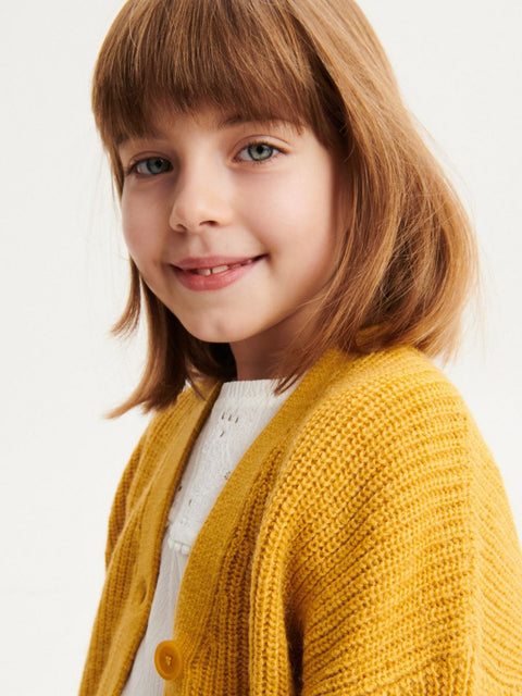 Young girl wearing a yellow cardigan on a plain background