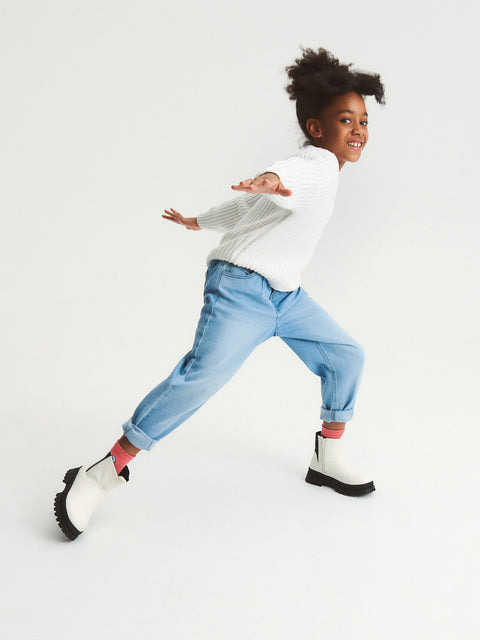 Child wearing a white sweater, light blue jeans, and white boots on a white background