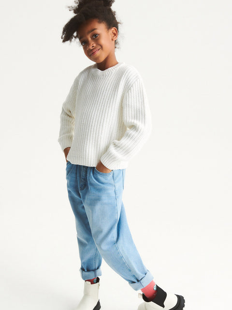 Child wearing a white sweater and light blue jeans on a white background