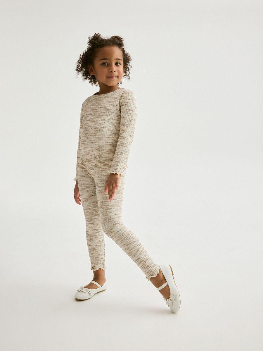 Child wearing a beige long-sleeve top and leggings on a white background