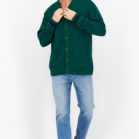 Man wearing a green varsity jacket, light blue jeans, and red sneakers on a white background