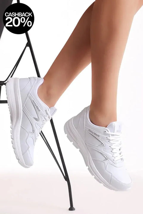 White sneakers worn by a person sitting on a black chair with a white background