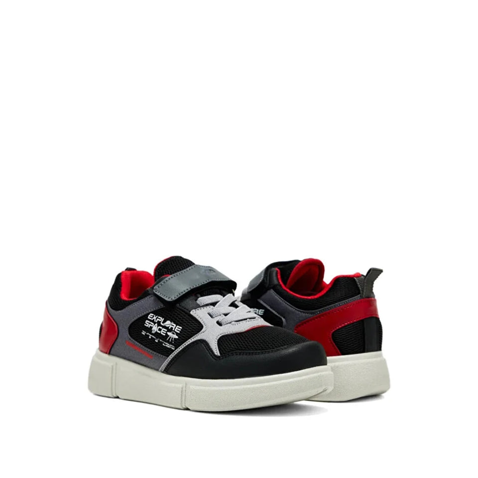 A pair of kids' sneakers in black, gray, and red, featuring a hook-and-loop strap, white laces, and a thick off-white sole. The brand name 'Explorers Direct' is visible on the side of the shoe.