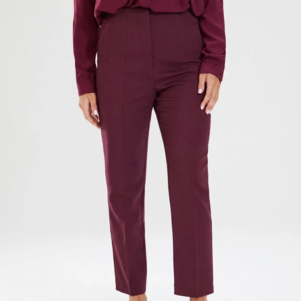 A model wearing a pair of high-waisted, straight-leg trousers in a deep burgundy color, paired with a matching long-sleeve top, against a plain light gray studio background.