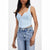 A woman wearing a light blue denim corset-style camisole top with lace-up front and ruffled trim, paired with light-wash distressed jeans, against a plain light gray background.