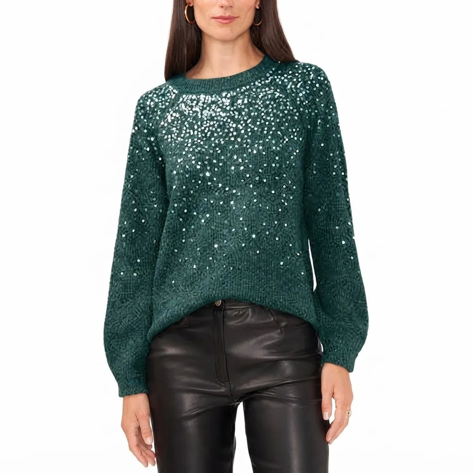 A woman wearing a dark green knit sweater covered in small white sequins, paired with black faux-leather pants, against a plain white background.