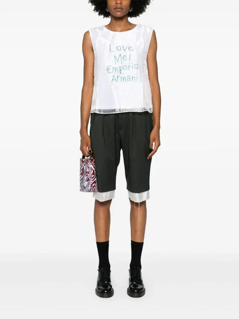 Person wearing a white sleeveless top with text and black shorts on a white background