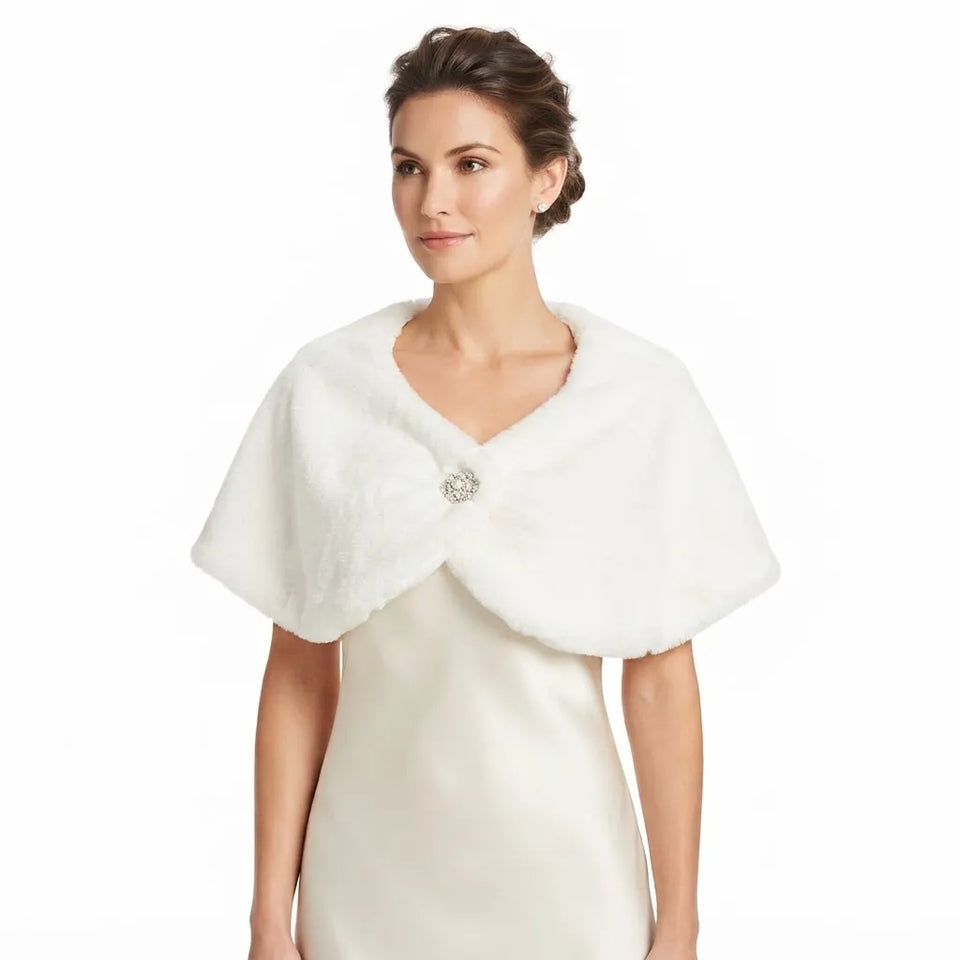 A woman wearing a white faux fur cape collar with a decorative crystal-embellished brooch, layered over a cream satin dress against a plain white background.