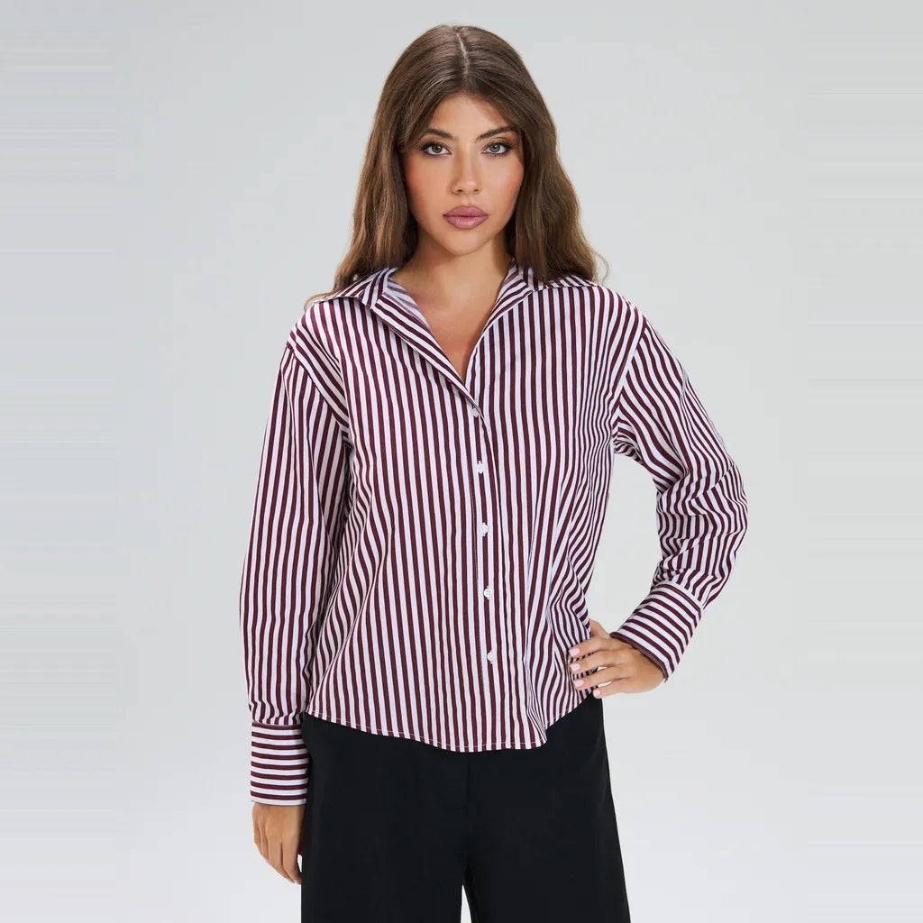 A woman modeling a long-sleeve button-up shirt with vertical burgundy and white stripes, paired with black pants, against a light gray studio background.