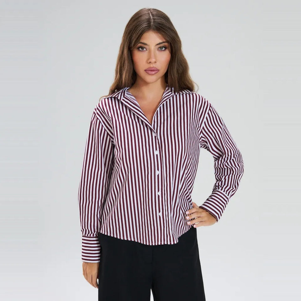 A woman modeling a long-sleeve button-up shirt with vertical burgundy and white stripes, paired with black pants, against a light gray studio background.
