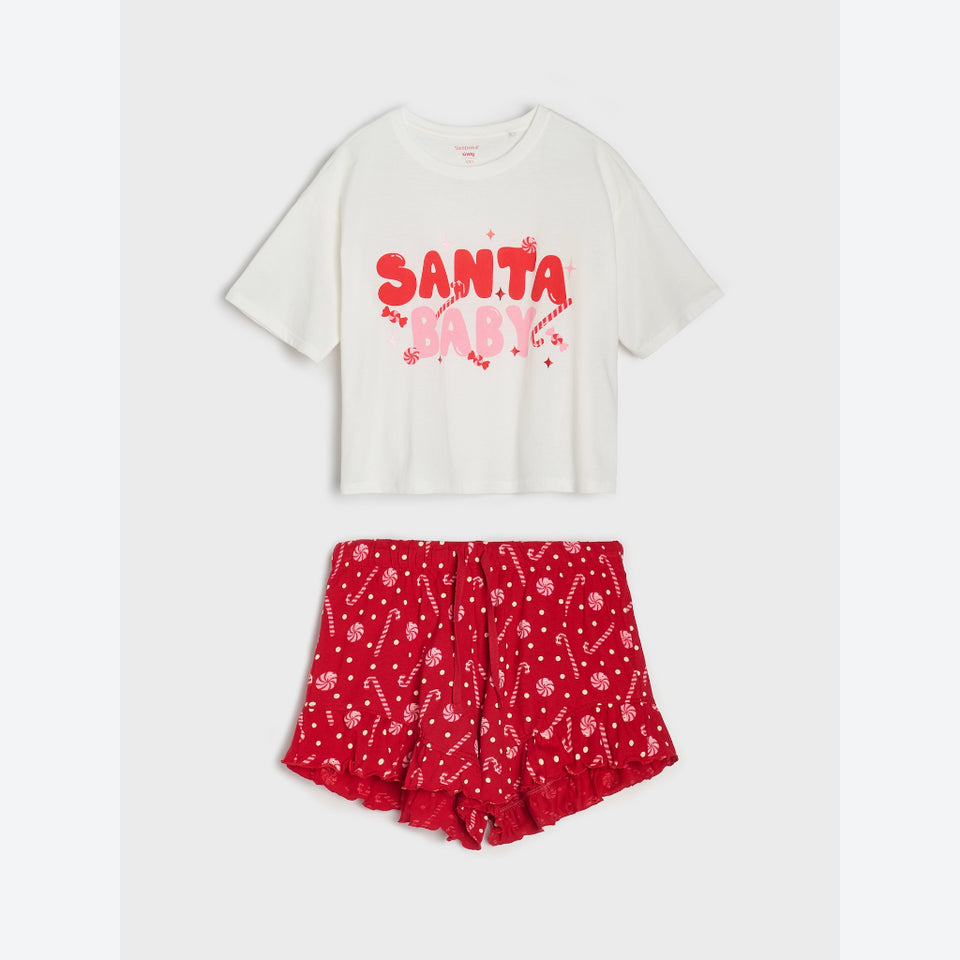 A two-piece kids' holiday pajama set featuring an off-white short-sleeve t-shirt with a red and pink 'SANTA BABY' graphic, paired with red ruffled shorts with a white candy cane and snowflake print.