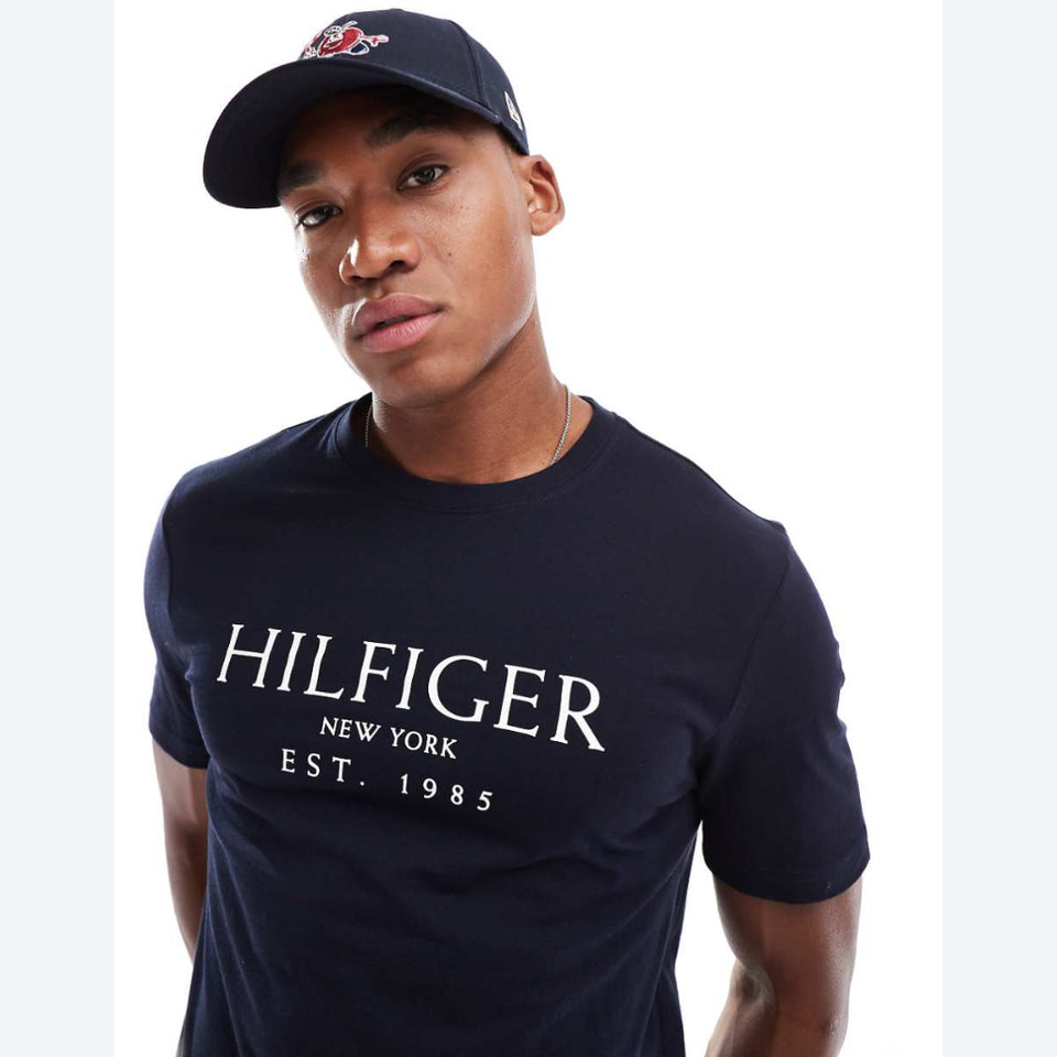 A man wearing a navy blue Tommy Hilfiger t-shirt and matching baseball cap, photographed against a clean white background.