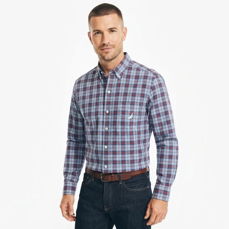 A man wearing a long-sleeve button-down plaid shirt in blue, red, and white, paired with dark jeans and a brown belt, photographed against a plain white background.