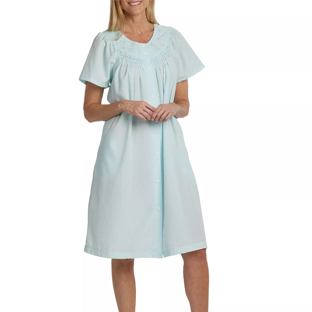 A woman modeling a light mint green short-sleeve nightgown with a smocked neckline, standing against a plain white background.