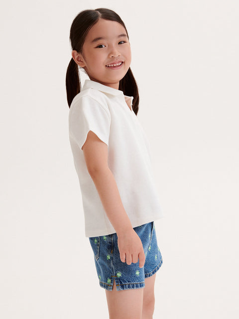 Young girl wearing a white polo shirt and denim shorts on a white background