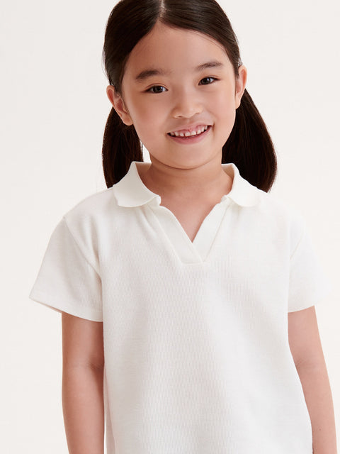 Young girl wearing a white polo shirt against a plain background