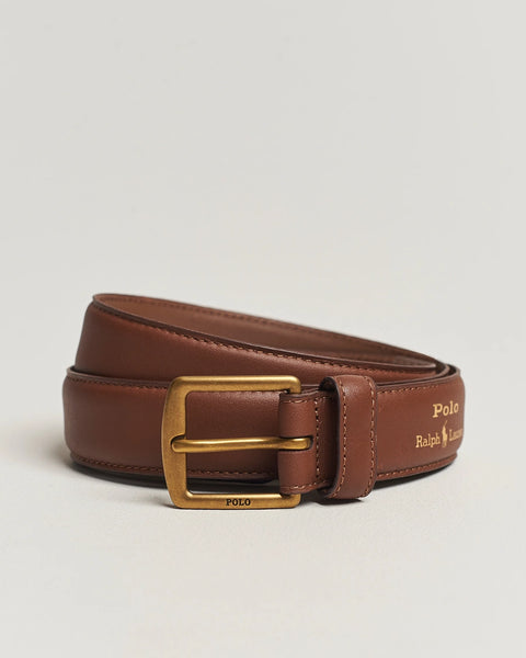 Brown leather belt with gold buckle on a light beige background