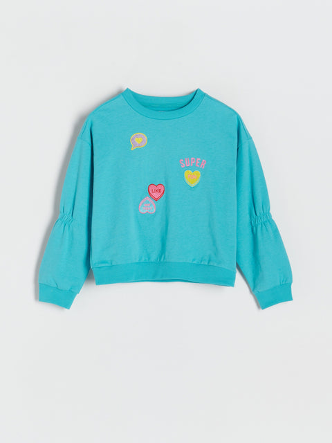 Turquoise sweatshirt with colorful graphics on a light gray background