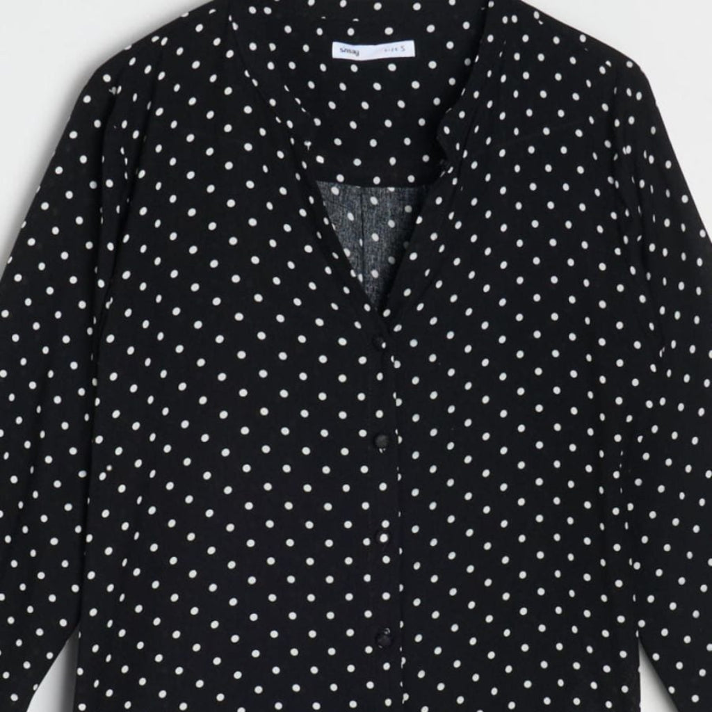A black long-sleeve blouse with a white polka dot pattern, featuring a V-neckline and button-front closure.